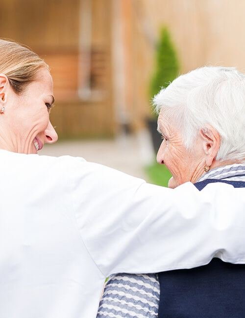 An older woman smiling warmly in conversation with her carer outdoors