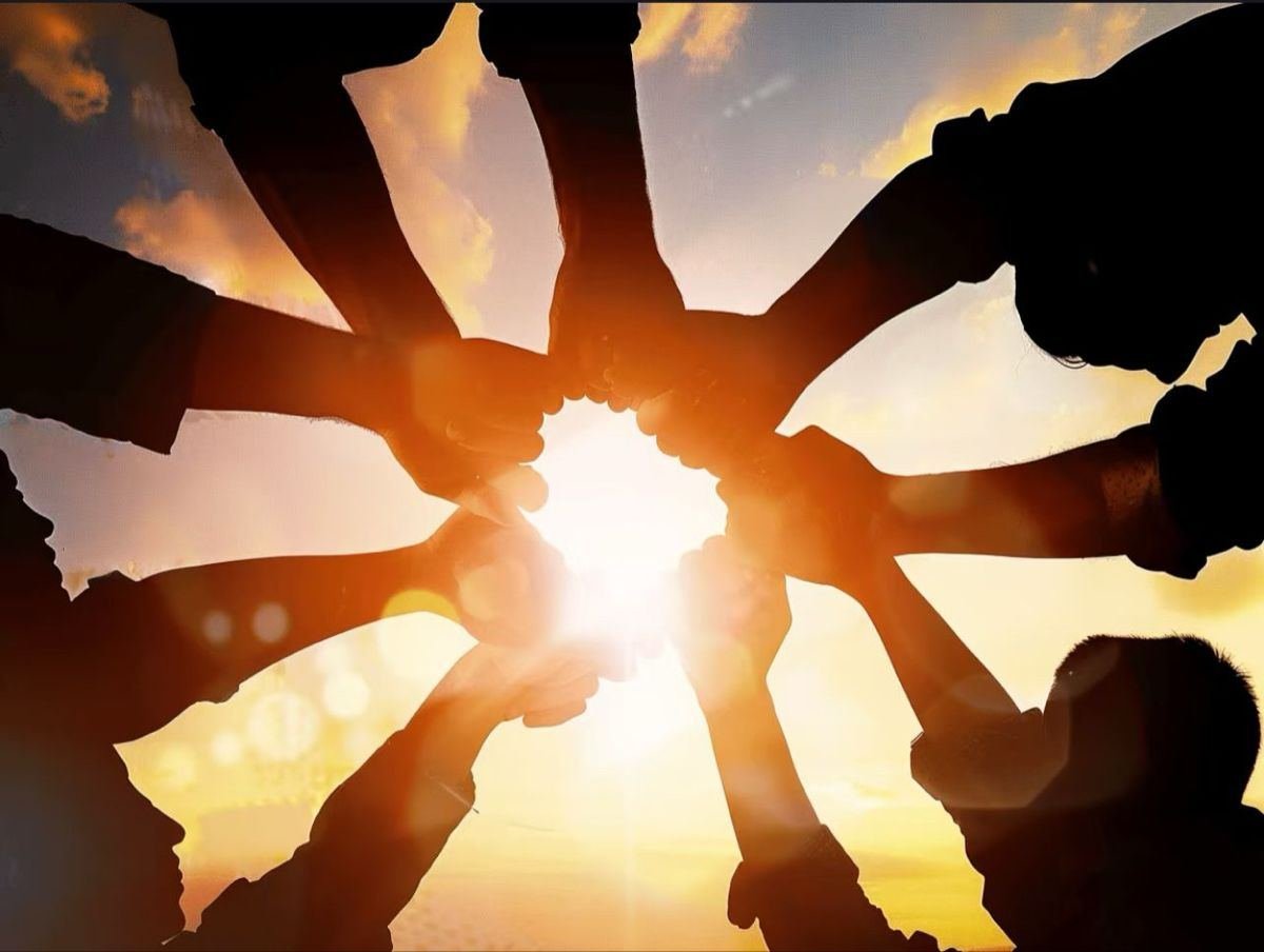 Silhouetted hands of the Obatos team joined together in a circle at sunset